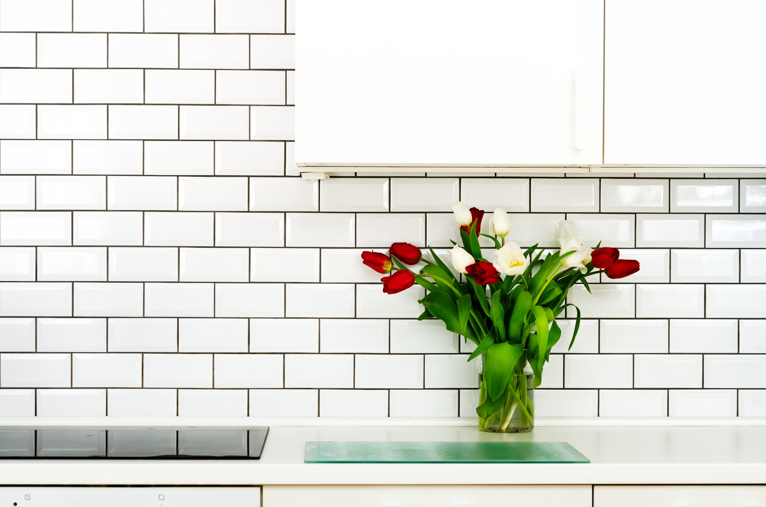 Fresh bouquet of red and white tulips on kitchen table. Detail of home interior, design. Minimalistic concept. Flowers for mother, girl, woman. Copy space