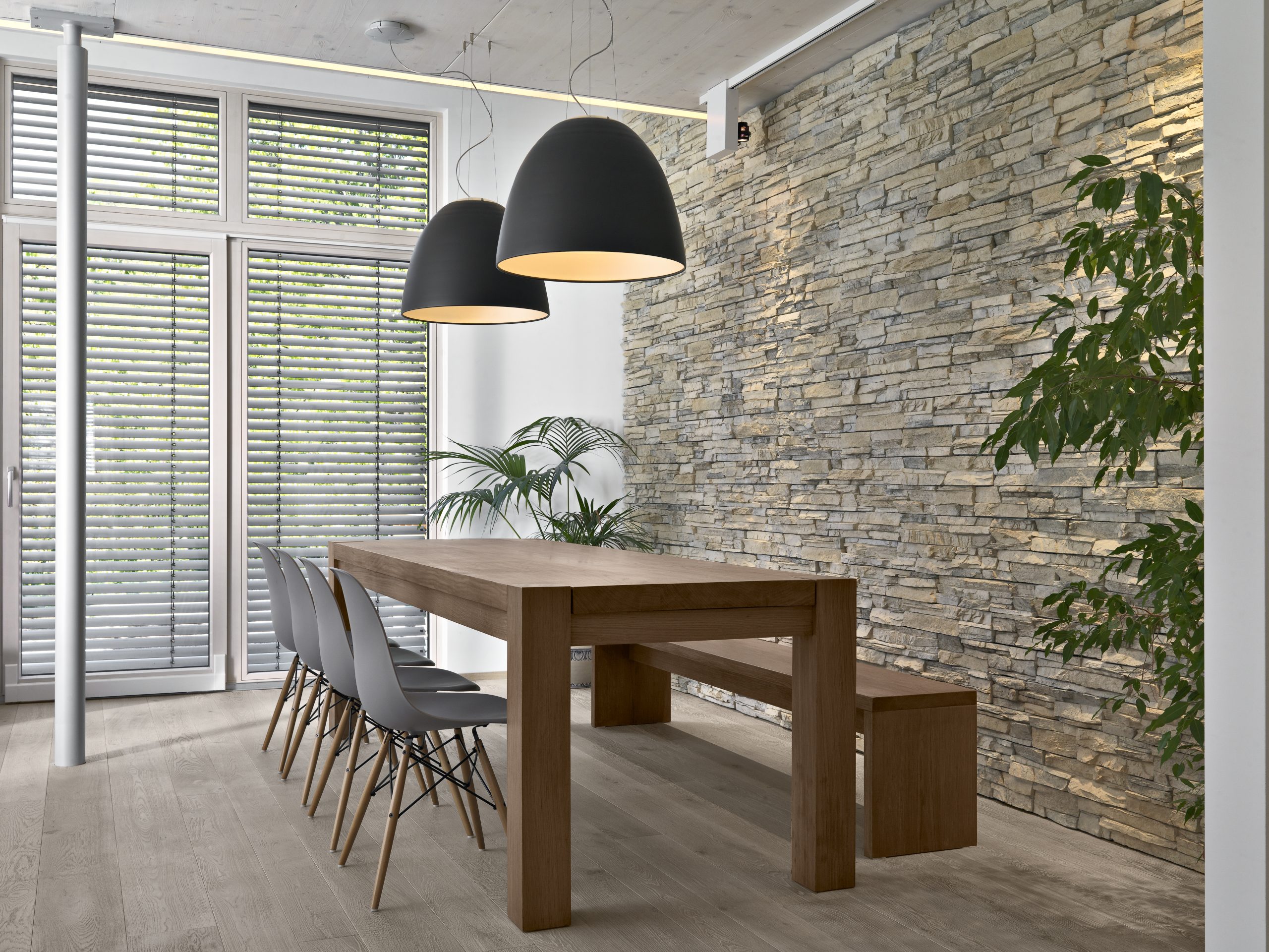 interior of the modern living room in the foreground there is a dining  table behind wich there is a stone wall, the floor is made of wood