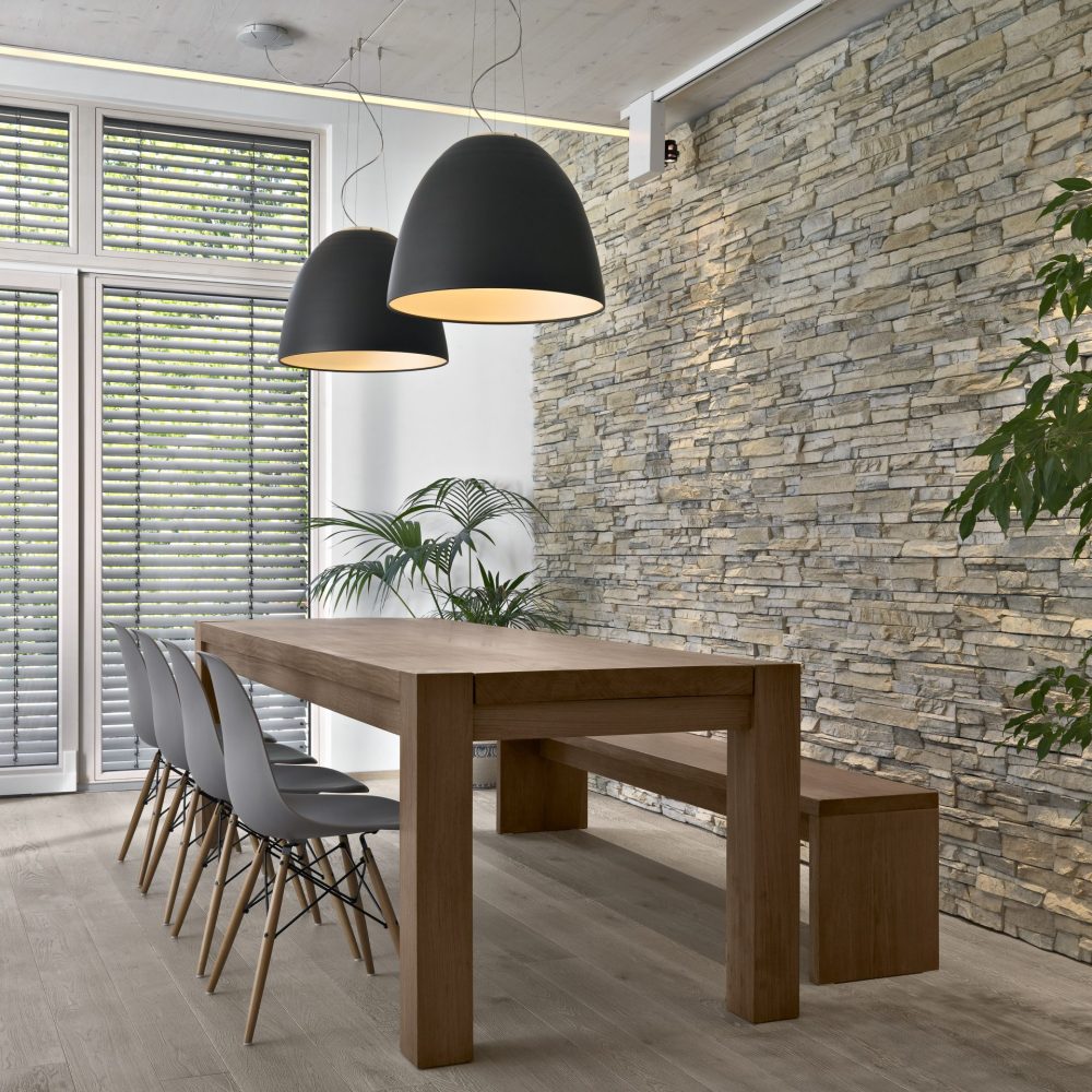 interior of the modern living room in the foreground there is a dining  table behind wich there is a stone wall, the floor is made of wood